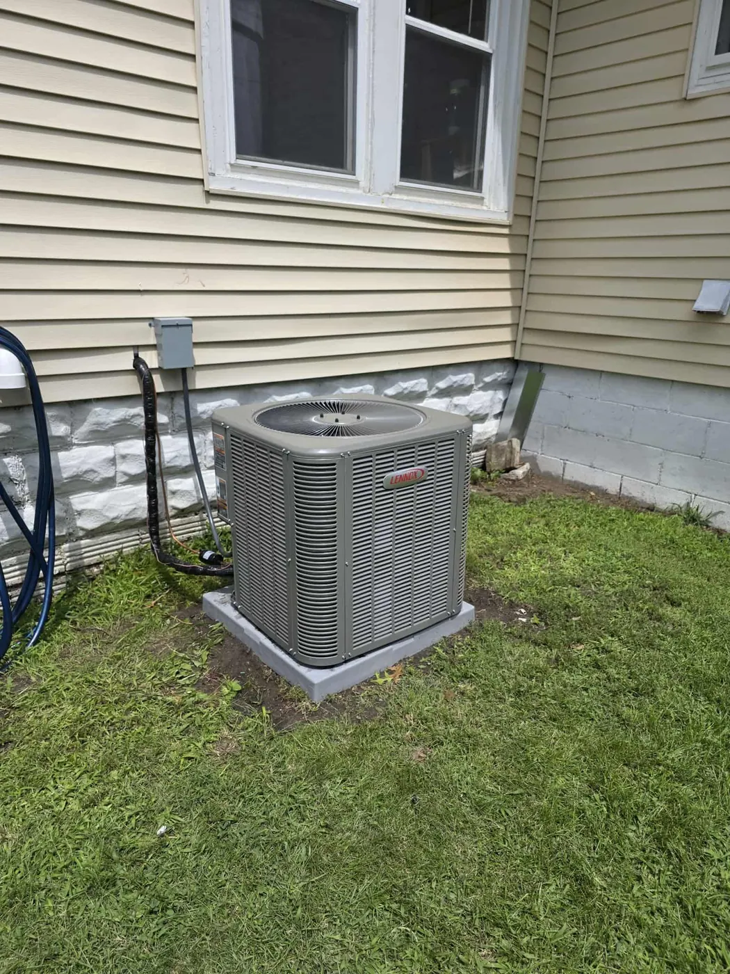 New central air conditioner condenser on a pad beside a house