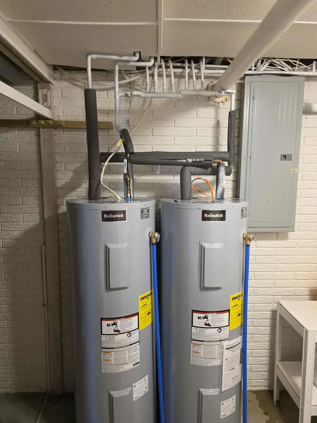Two new electric water heaters installed side by side in a basement